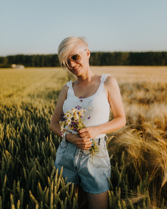Atraktivní blondýnka s kyticí heřmánku v pšeničném poli