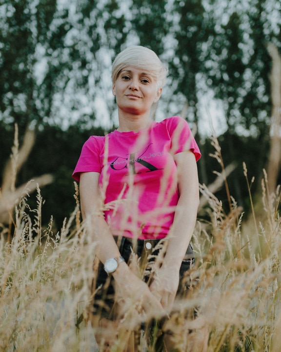 Růžová dáma v efektní narůžovělé košili a černých kalhotách v travních porostech