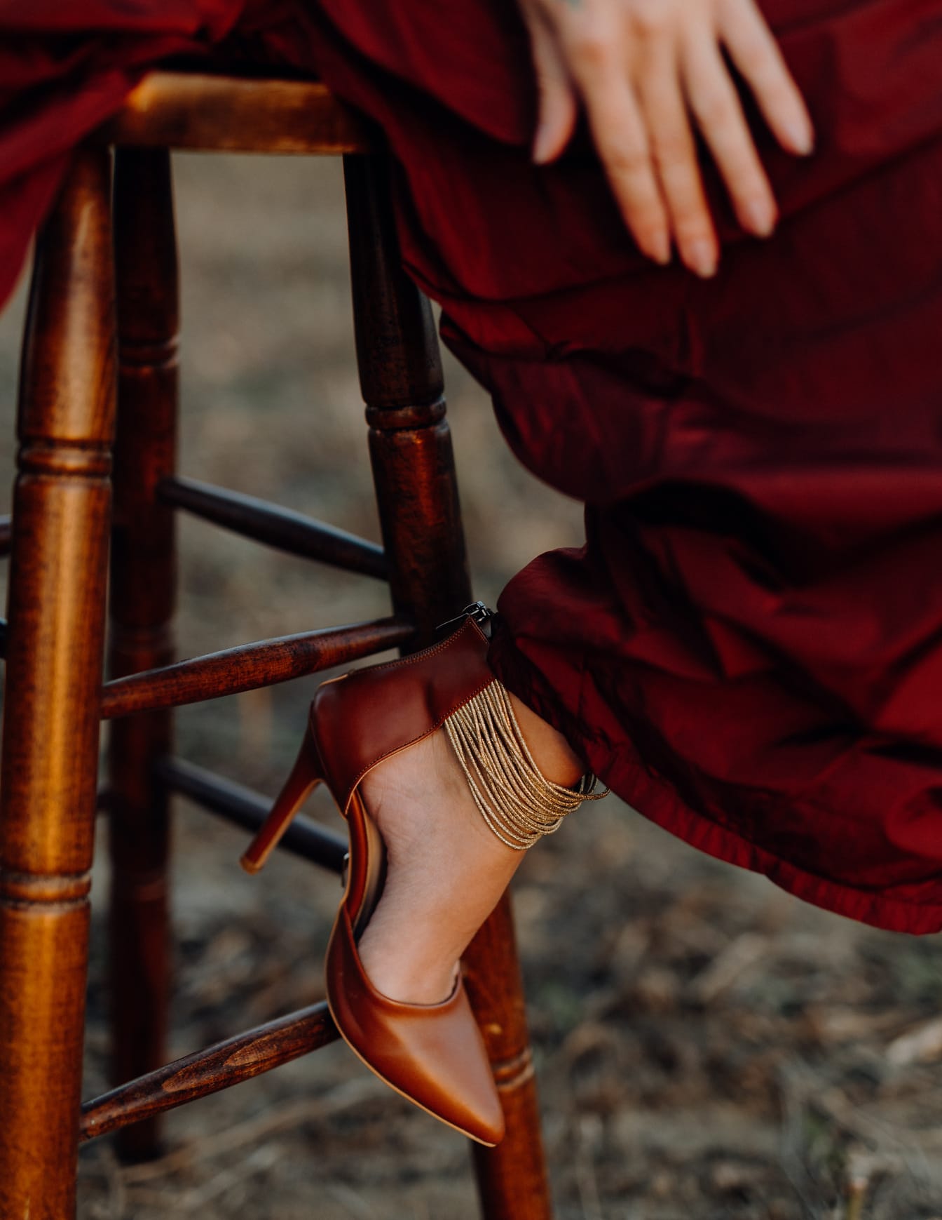Dunkelrote Sandale am Bein einer Frau im roten Kleid, die auf einem Hocker sitzt