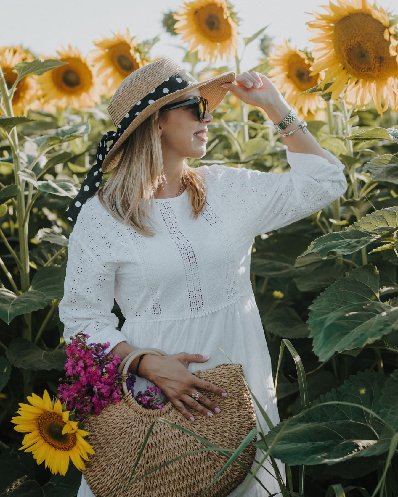 Uśmiechnięta młoda kobieta w słomkowym kapeluszu i wiklinowym koszu na polu słoneczników