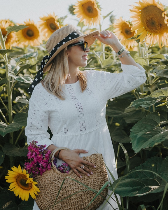 Usmívající se mladá žena se slaměným kloboukem a proutěným košem ve slunečnicovém poli