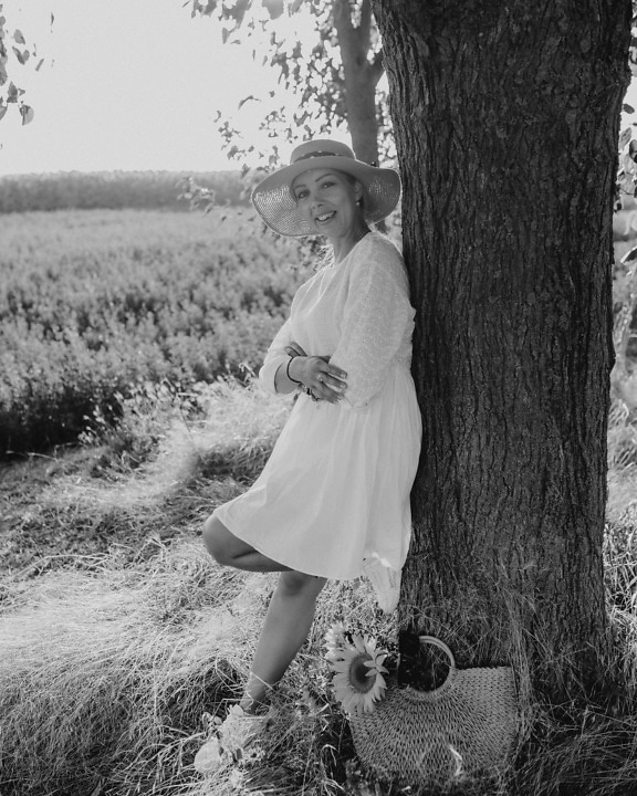 Monochrome portrait of woman in straw hat and white dress in coutryside