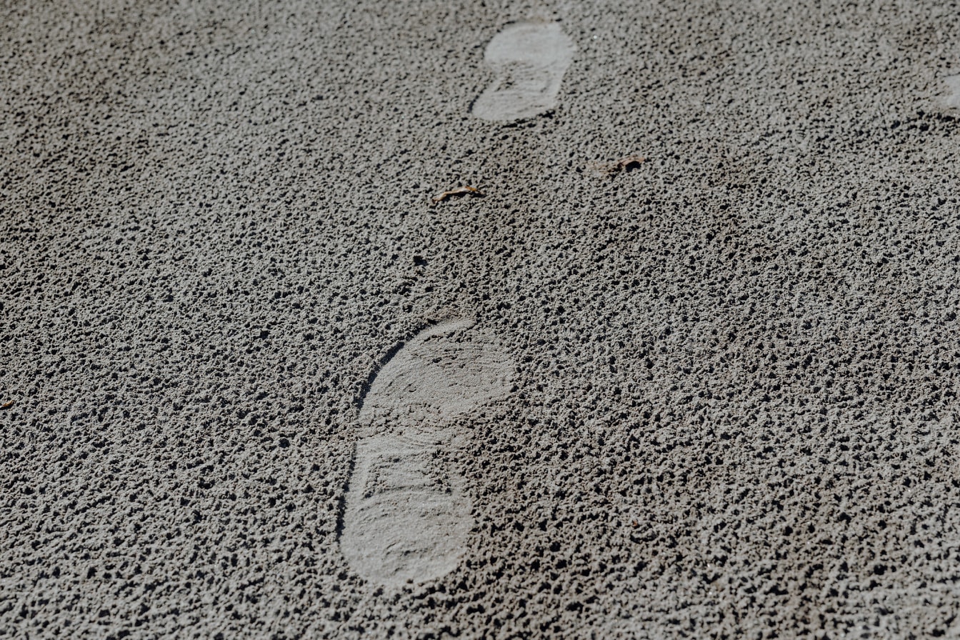 Pași pe textura apropiată a suprafeței nisipului gri