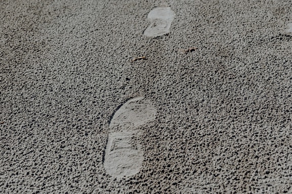 Footsteps on grey sand surface close-up texture