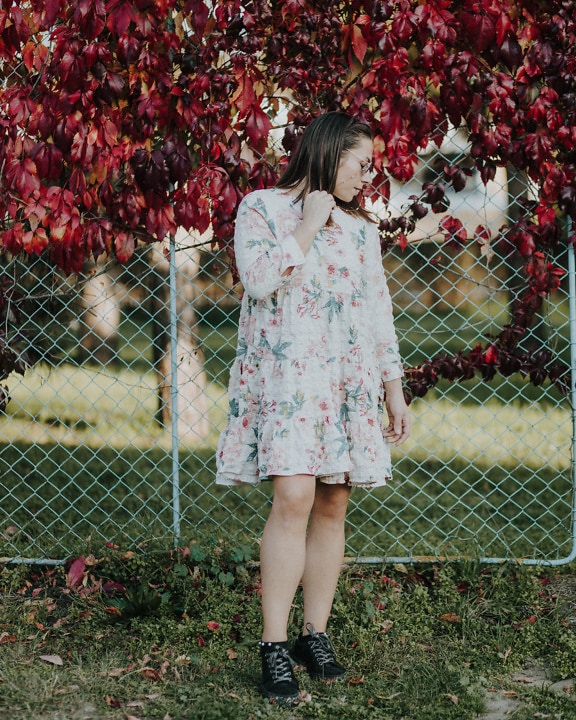Brunette in colorful floral dress posing by fence