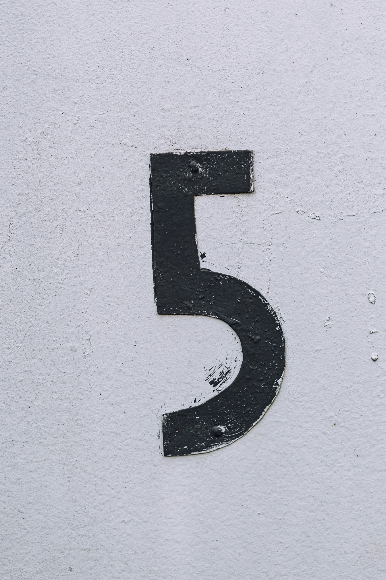 Cat hitam pada logam nomor 5 pada tekstur close-up dinding putih