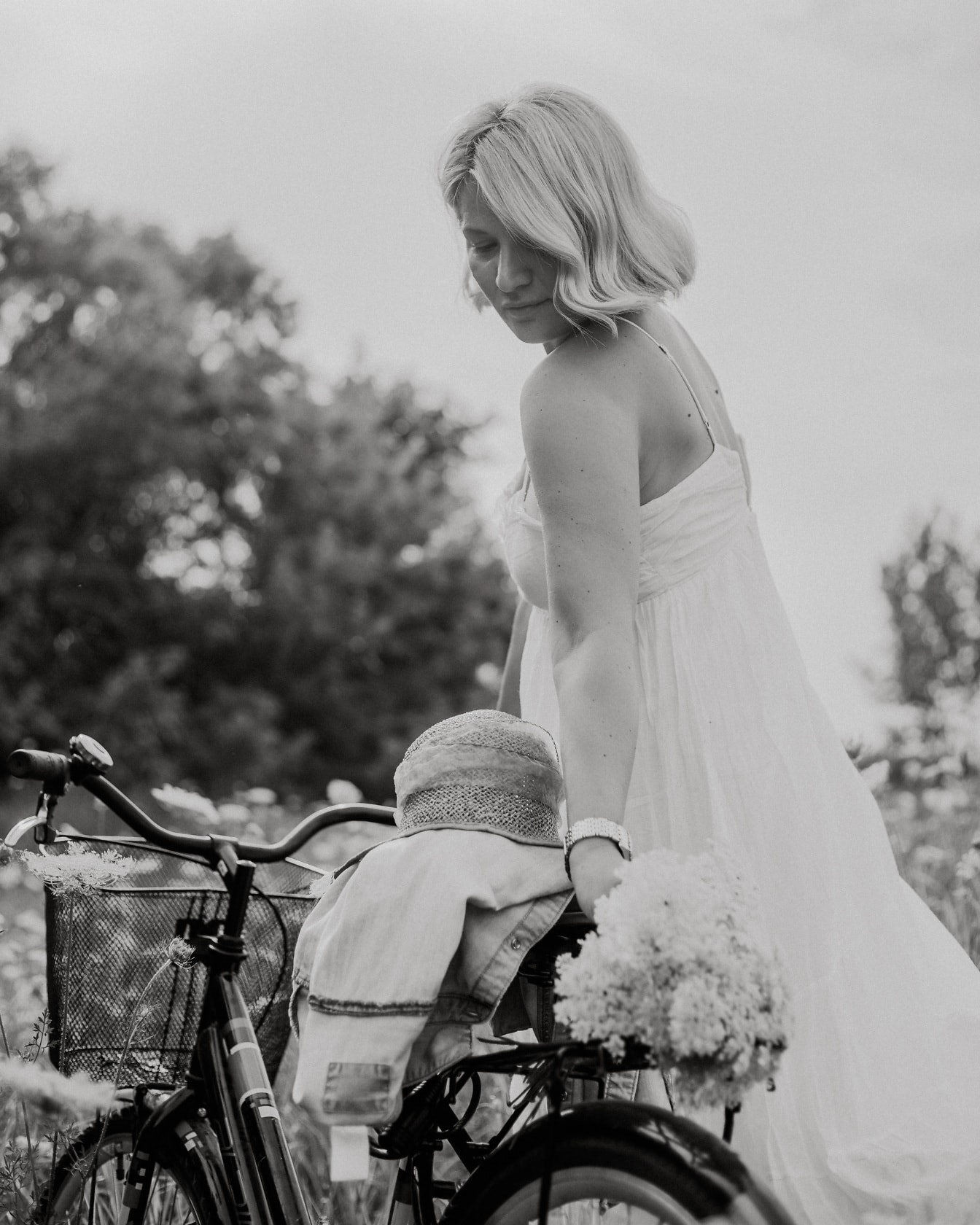 Snygg blondin i vit klänning för tappning med cykel på landsbygden monokromt foto