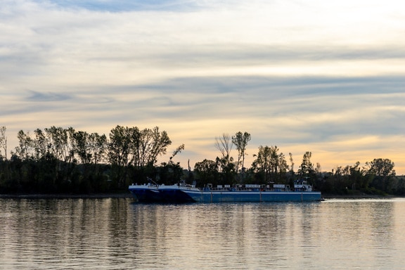 Gammelt mørkeblåt fragtskib i skumringen på Donau-floden