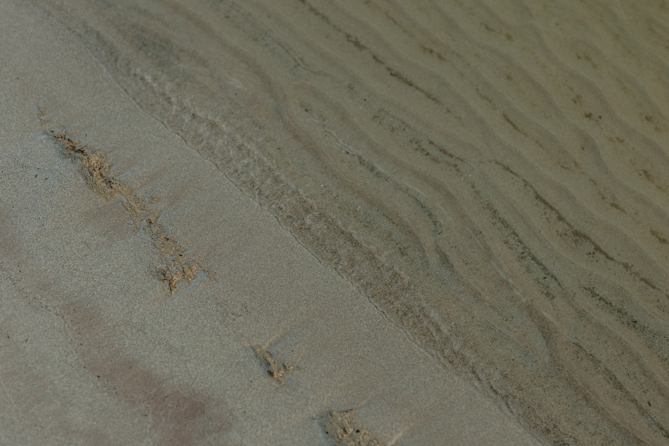 Mokrý piesok na pobreží a pod vodou s textúrou vĺn