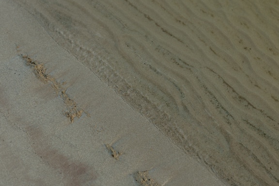 Våt sand på kysten og under vann med tekstur av bølger