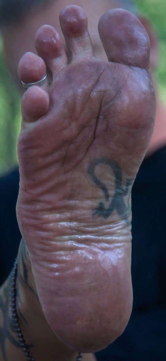 Barefoot man close-up of dirty foot with tattoo and ring