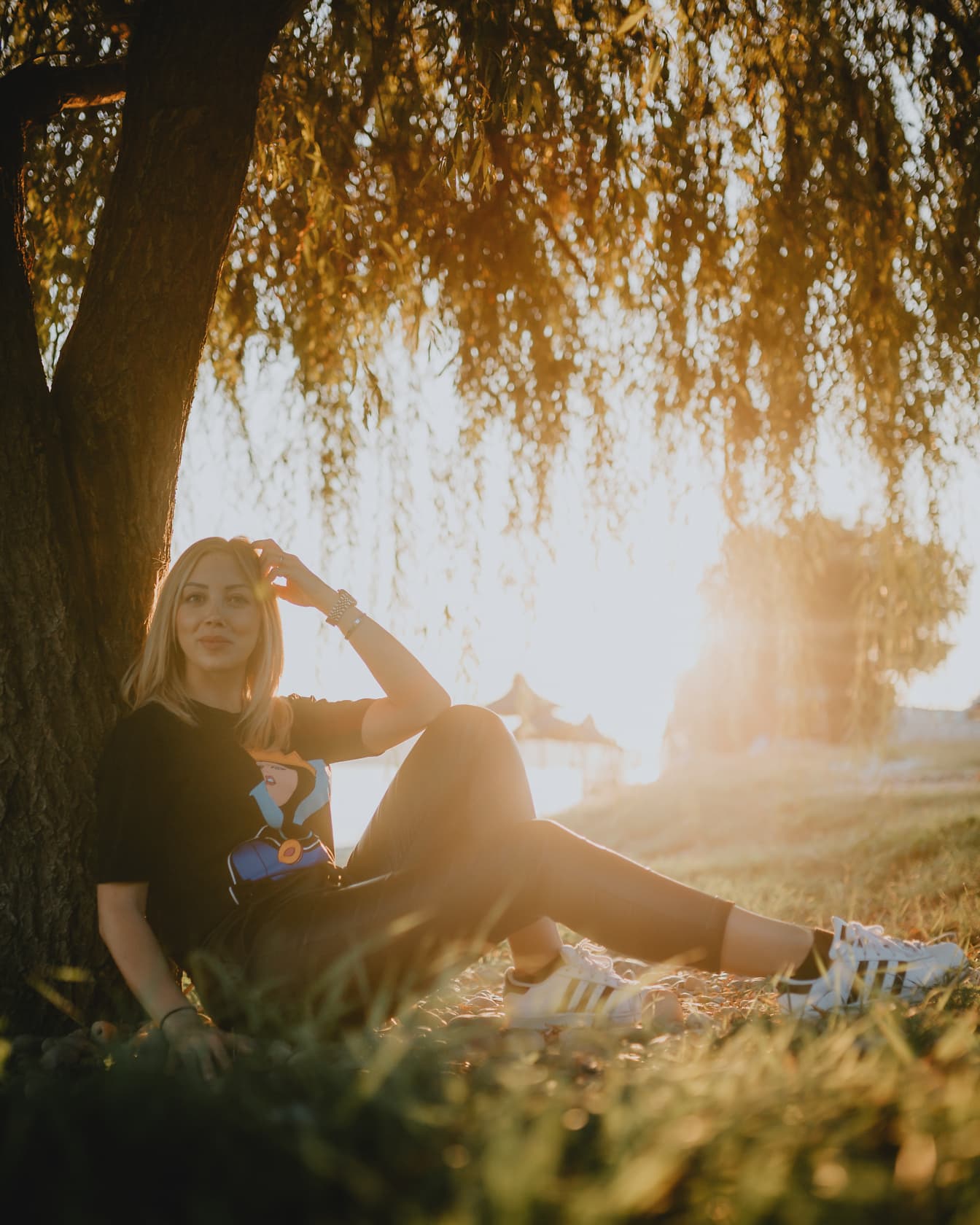 Atrakcyjna blondynka siedząca pod drzewem i pozująca o zachodzie słońca