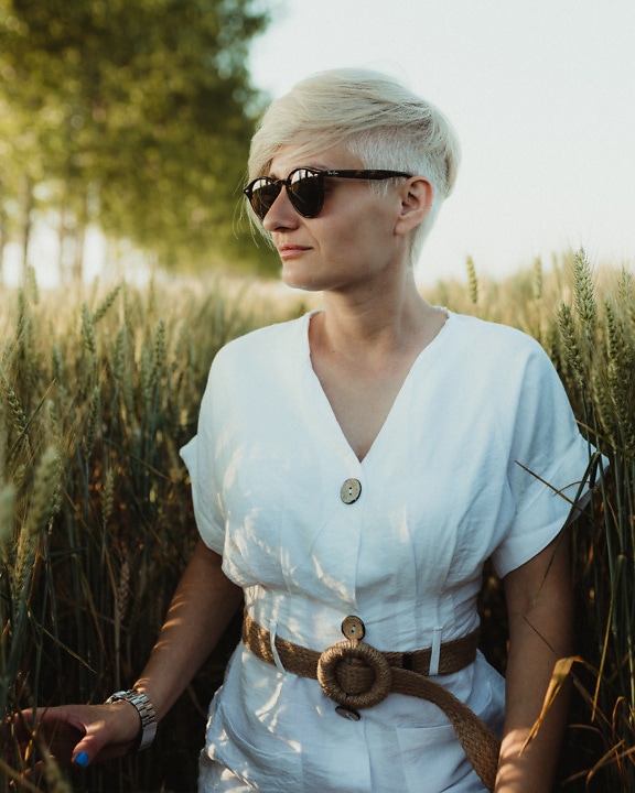 Blondine mit kurzen Haaren und Sonnenbrille posiert im Weizenfeld