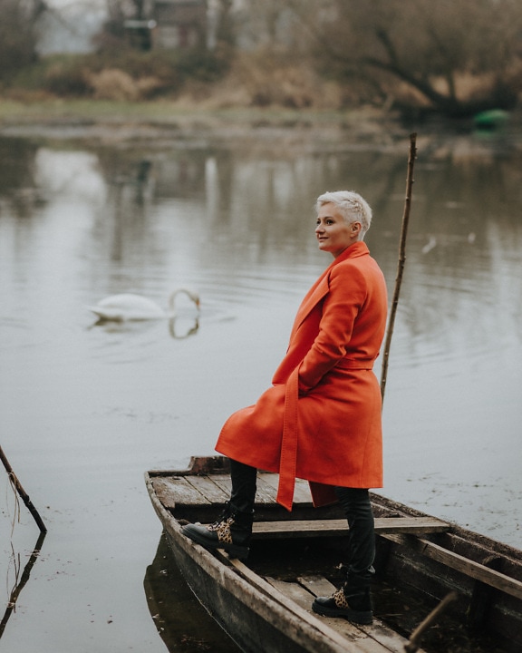 Attraktive Blondine mit kurzen Haaren im orangegelben Mantel steht im Boot