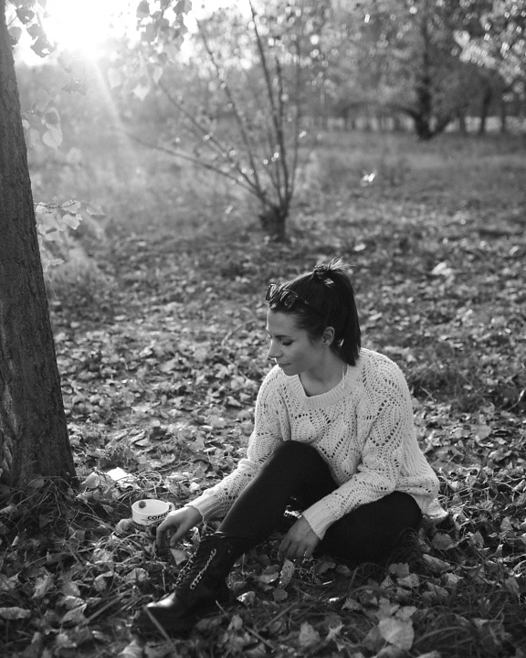 Mladá žena sedí venku ve vlněném svetru a užívá si slunečného dne