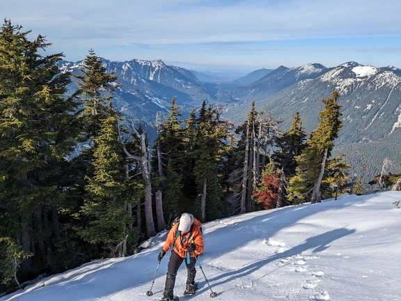 Randonneur grimpant sur une montagne enneigée avec panorama de la vallée en arrière-plan