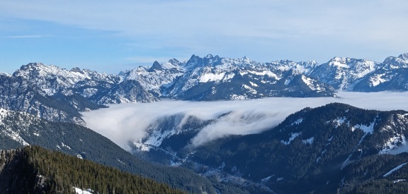 Ködös felhők panorámája a völgyben, háttérben fagyott hegycsúcsokkal