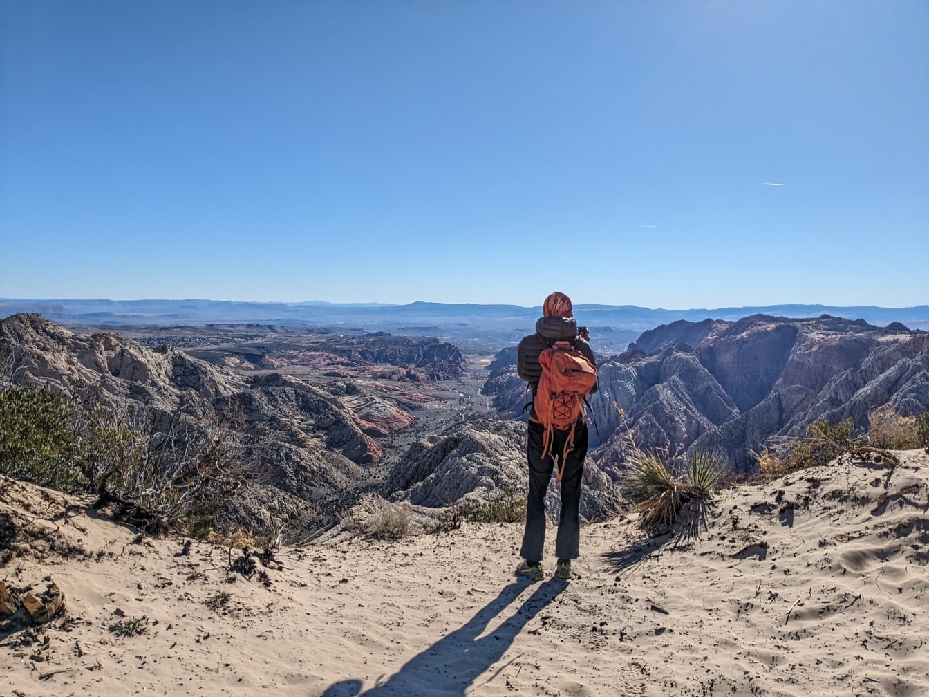 砂漠の崖の上に立って砂漠の渓谷のパノラマを楽しむバックパッカーハイカー