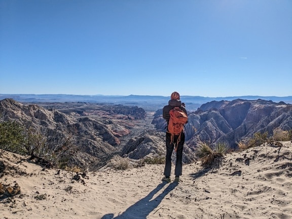 Người đi bộ ba lô đứng trên vách đá sa mạc và tận hưởng toàn cảnh thung lũng sa mạc