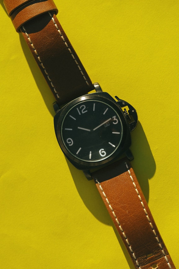 Old fashioned wristwatch with brown leather belt on yellow background close-up