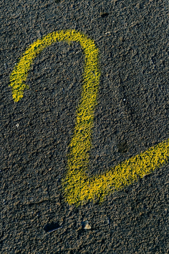 Numer dwa w żywej żółtej farbie na ciemnej fakturze betonu z bliska
