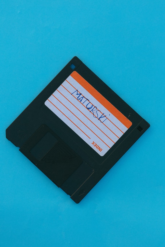 Old fashioned data storage floppy disk on blue background close-up photo
