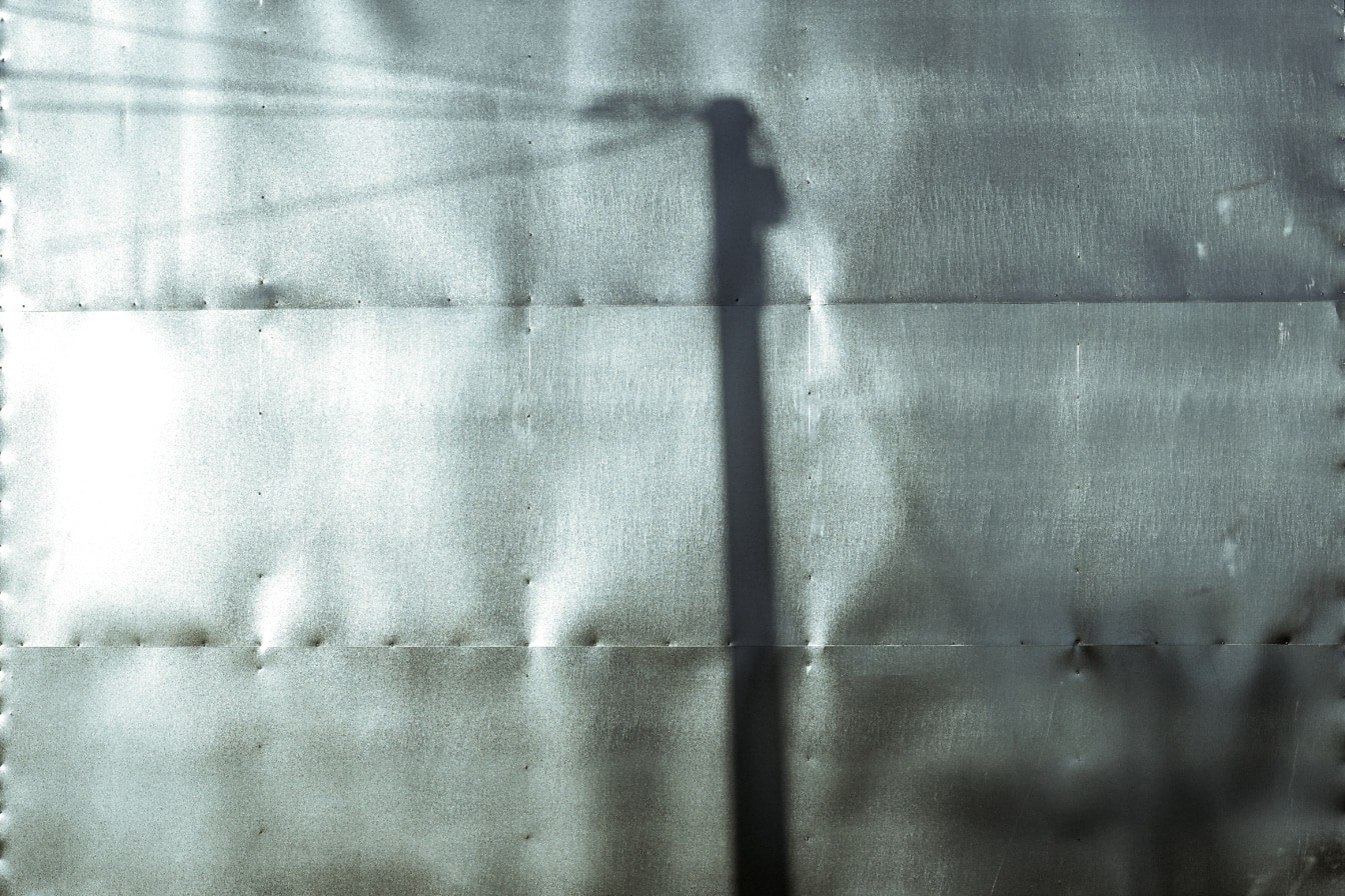 Tieň tieňa telefónneho stĺpa na kovovom povrchu monochromatická fotografia