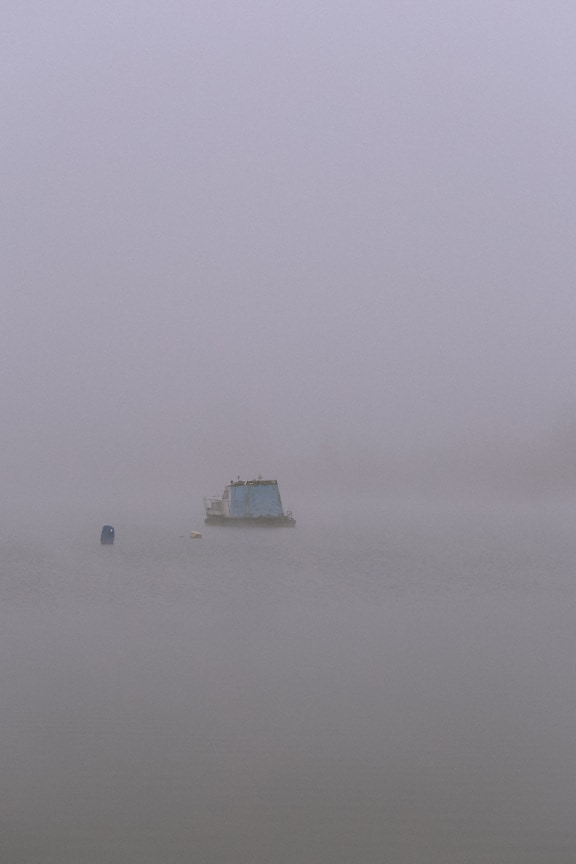 Small blue fishing boat on water on foggy day