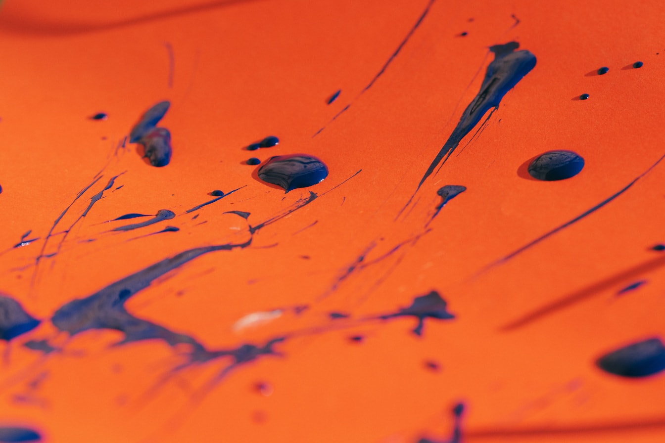Close-upfoto van donkerblauwe waterverfplons op oranje geel papier