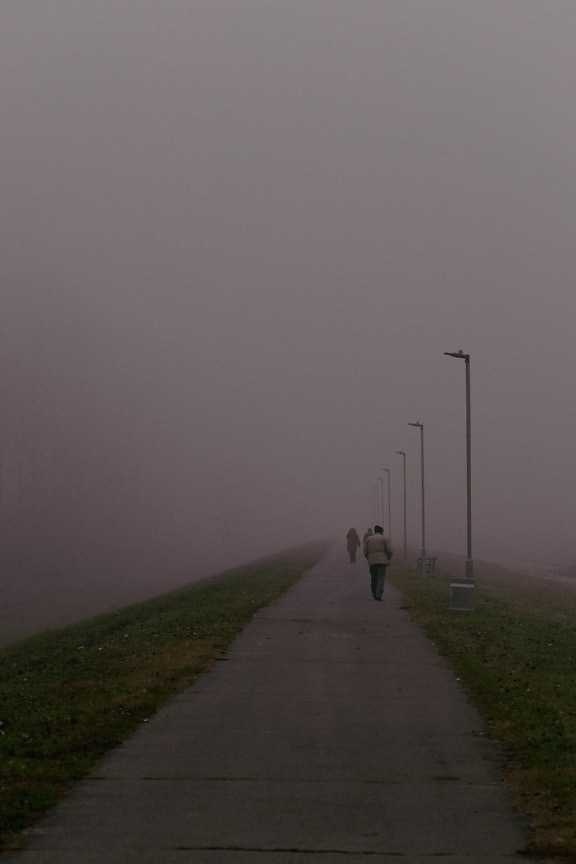 Pedestrian walking on foggy asphalt road in morning