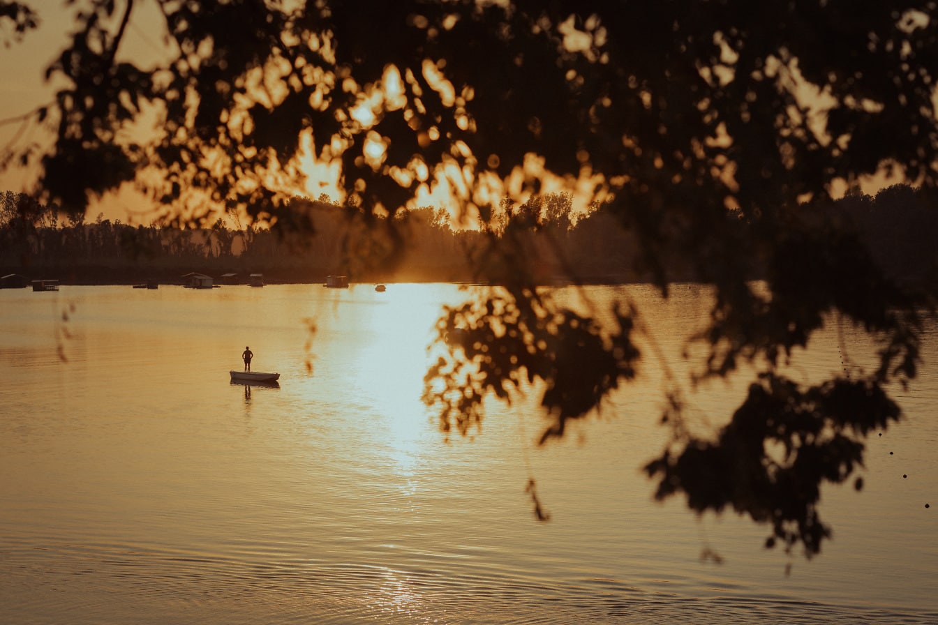 A tavon csónakban álló személy sziluettje naplementekor
