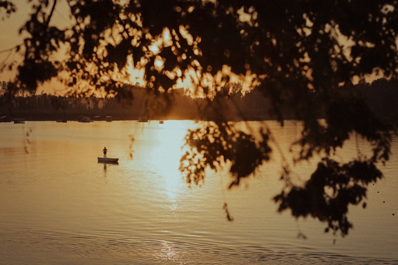 Siluetti henkilöstä, joka seisoo veneessä järvellä auringonlaskun aikaan