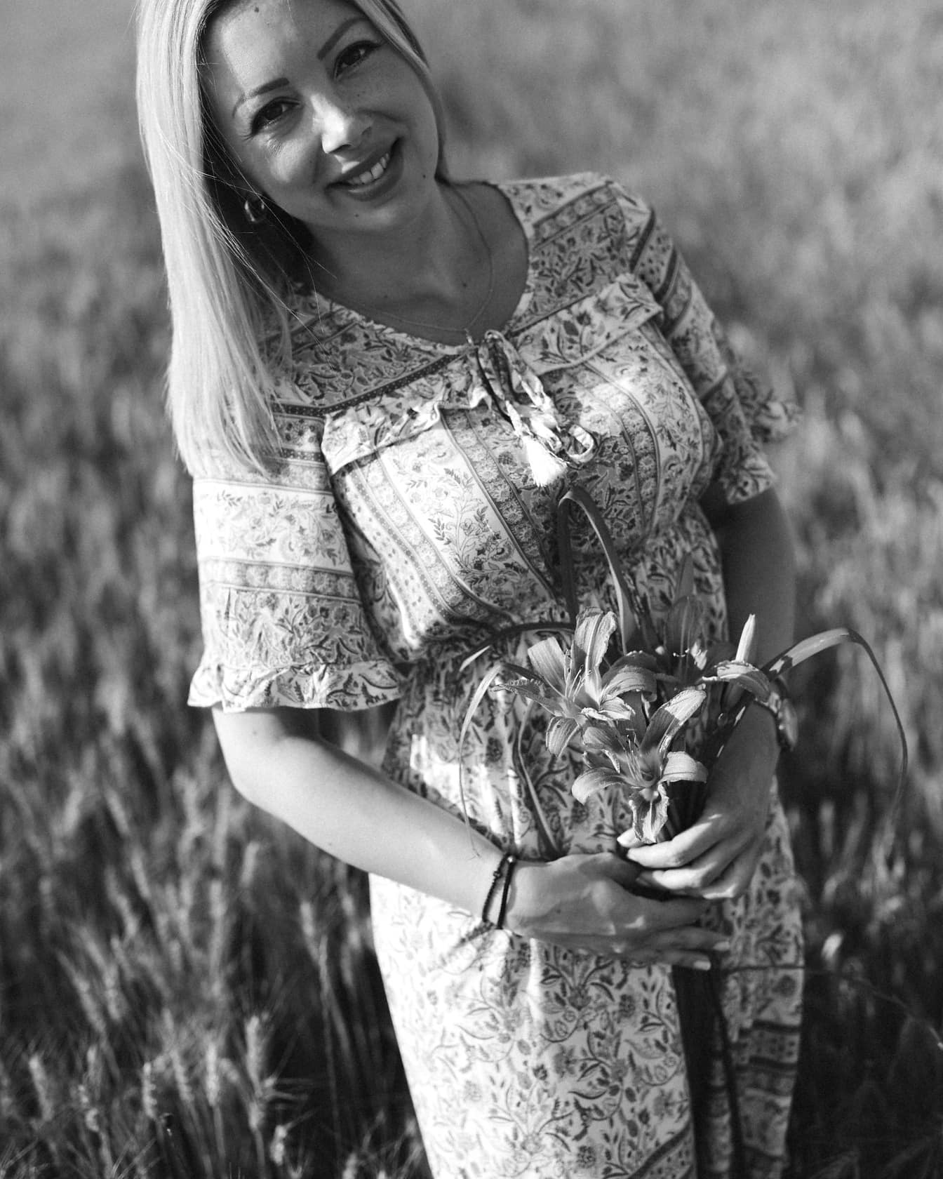 Monochromatyczny portret wspaniałej blondynki z kwiatami lilii na polu pszenicy