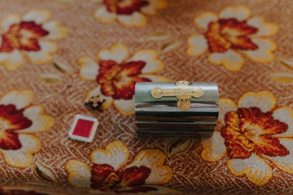Religious shining metallic chest with golden shine cross on orange yellow tablecloth