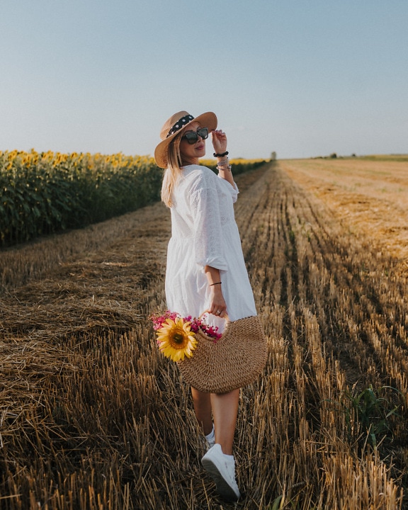 Krásná venkovská kovbojka se slaměným kloboukem a proutěným košem v pšeničném poli
