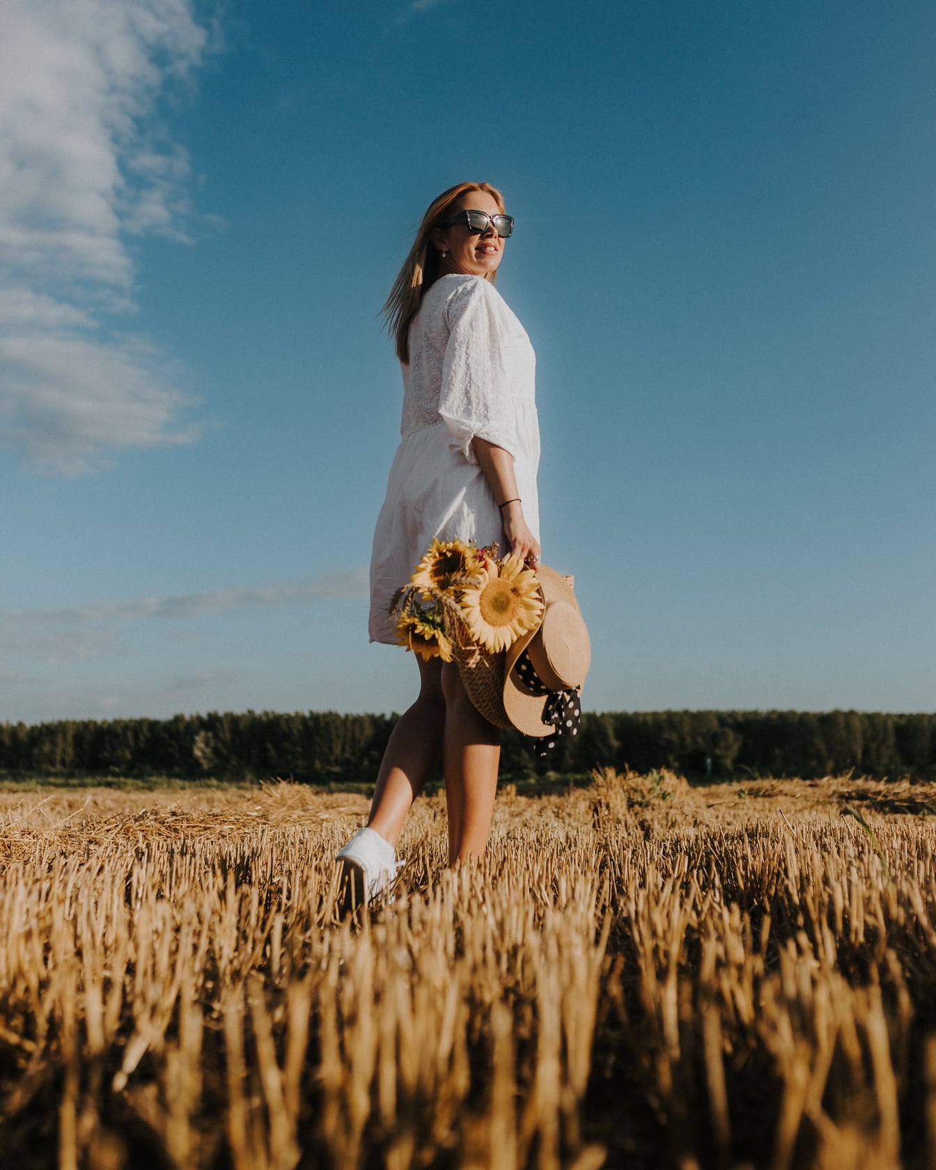 Cô gái tóc vàng hấp dẫn trên cánh đồng lúa mì với mũ rơm và giỏ đan bằng liễu gai