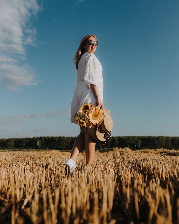 Jolie blonde dans un champ de blé avec un chapeau de paille et un panier en osier