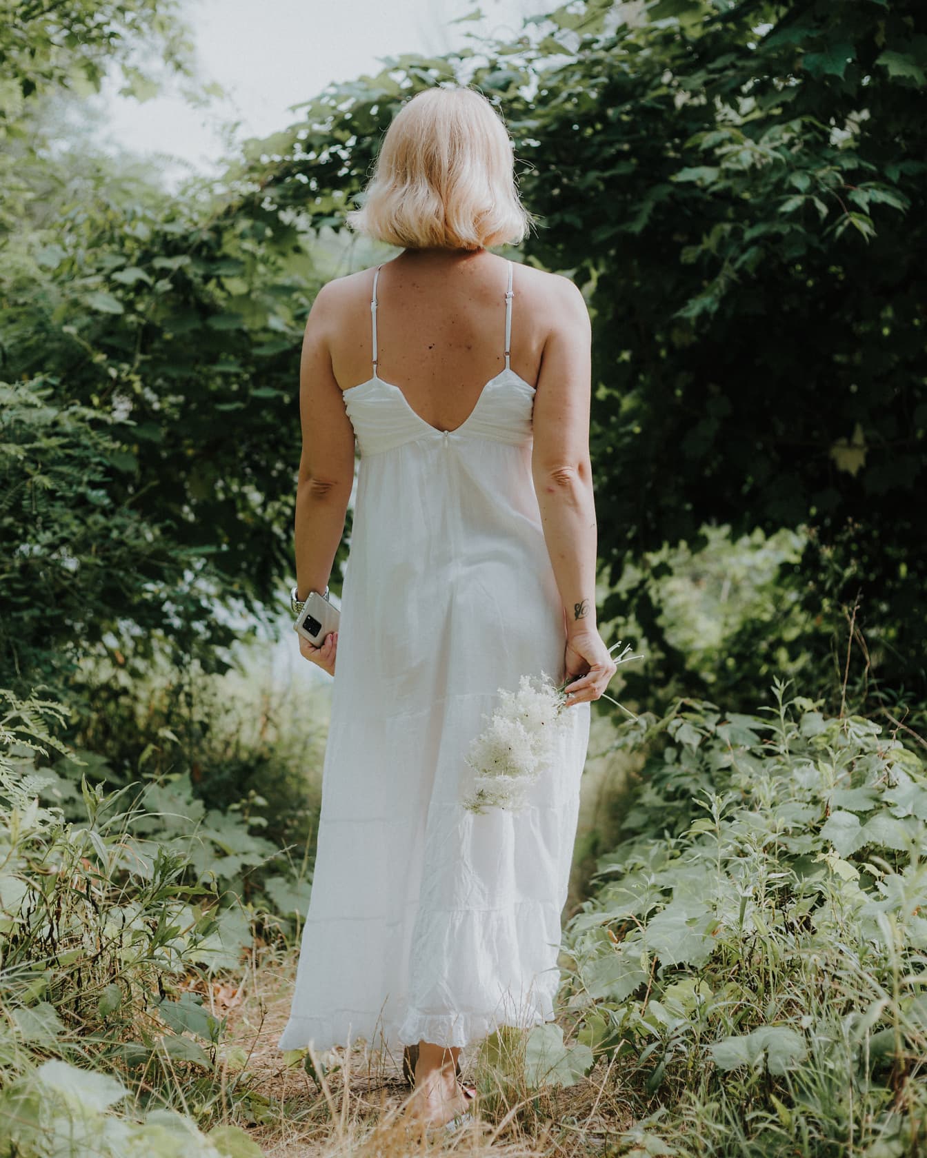 Elegant white cotton dress on young blonde walking in forest