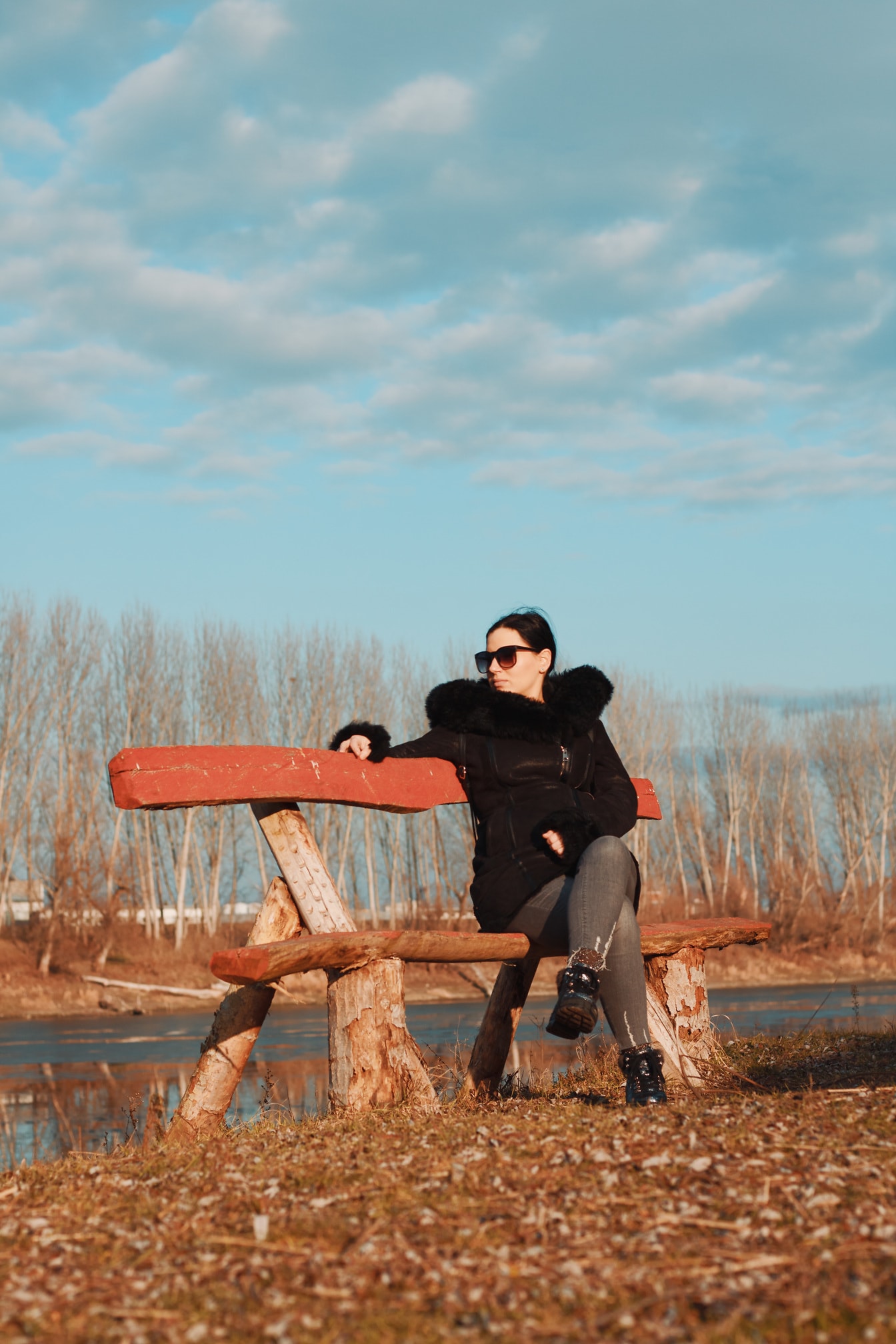 Brunetka mladá žena sedí na drevenej lavici v čiernej bunde