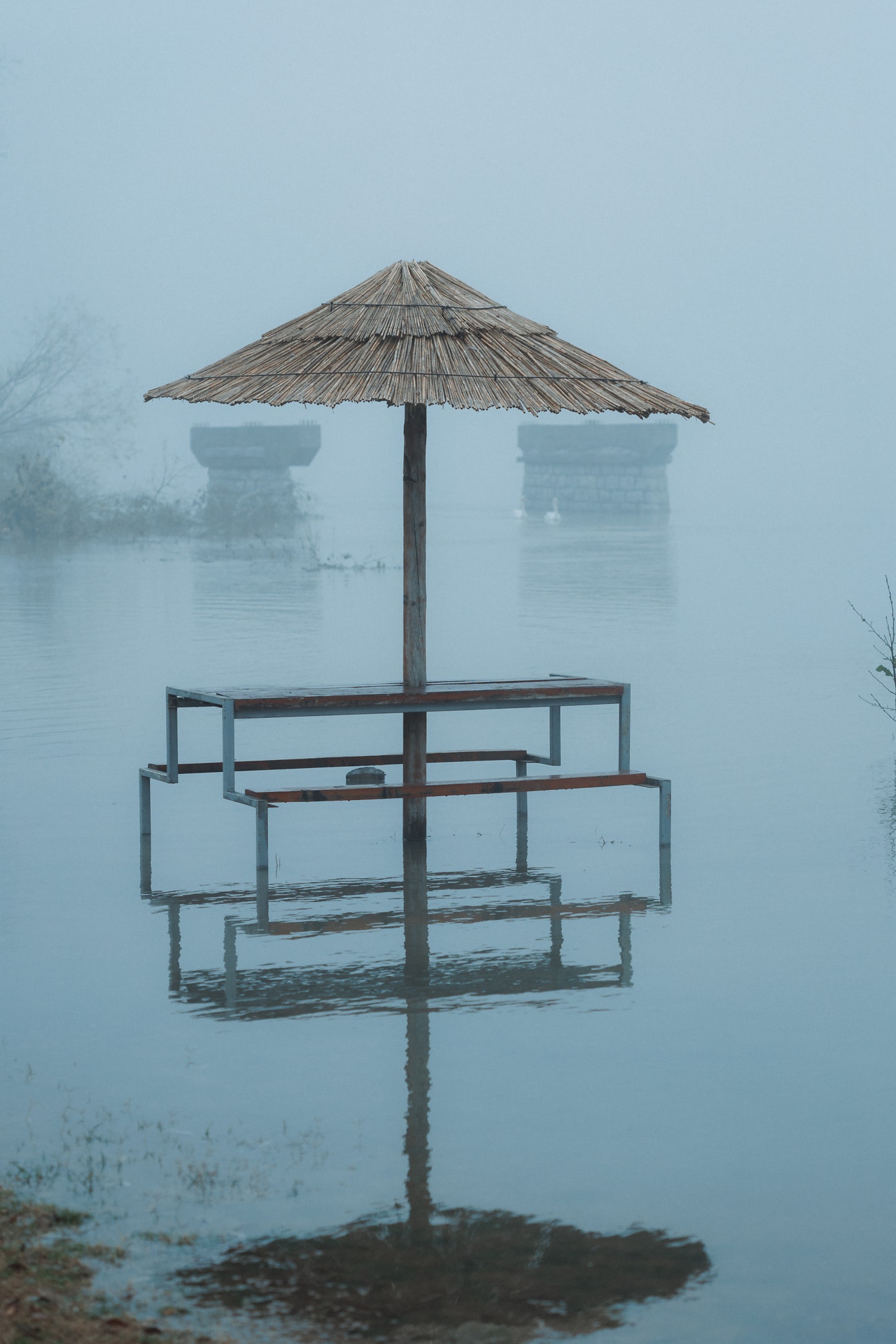 Overstroomde rivieroever met parasol in water op mistige dag