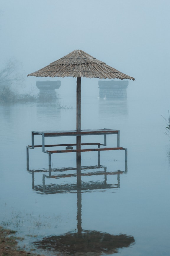 Elárasztott folyópart napernyővel a vízben ködös napon