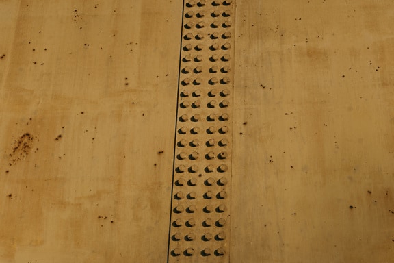 Tekstur af gulbrun maling på metal med store støbejernsskruer