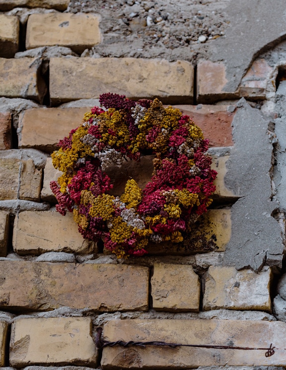 Αποξηραμένο στεφάνι λουλουδιών σε τραχύ τοίχο από τούβλα