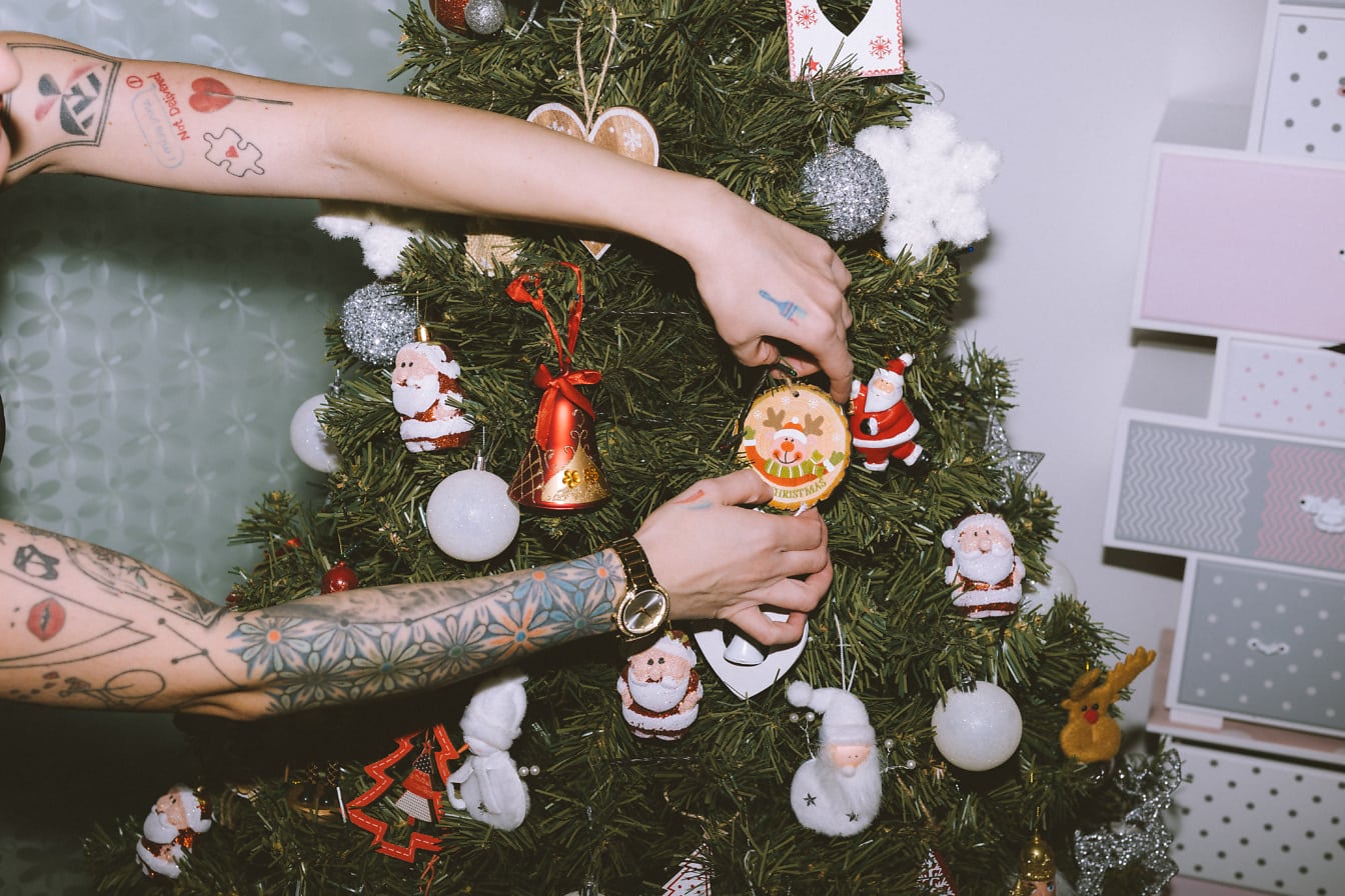 Persoană cu tatuaje pe mâini care decorează un pom de Crăciun