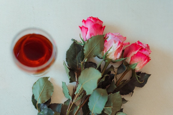 Kytica troch ružových ruží a pohár červeného vína na stole