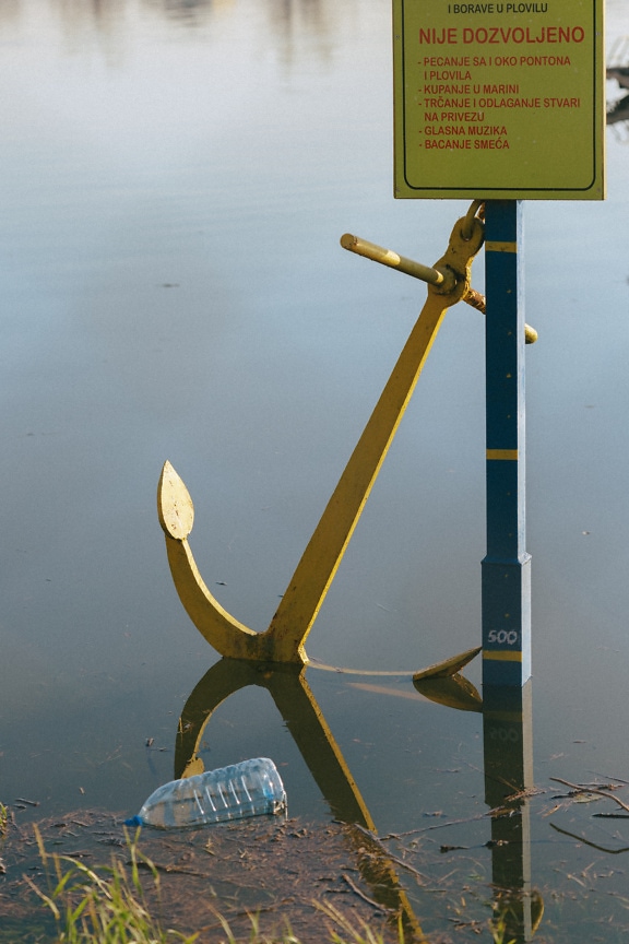Yellow cast iron anchor in water with warning sign