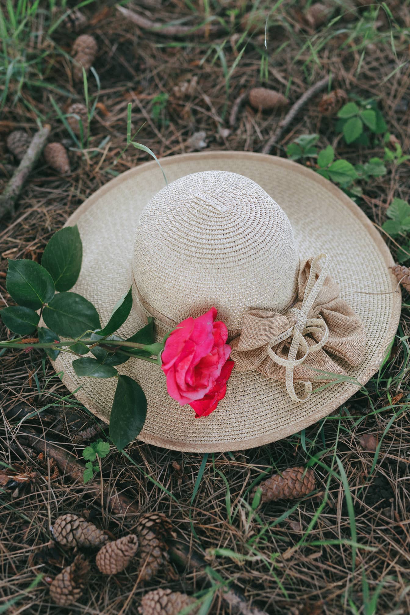 Topi jerami buatan tangan di tanah dengan mawar merah muda di atasnya