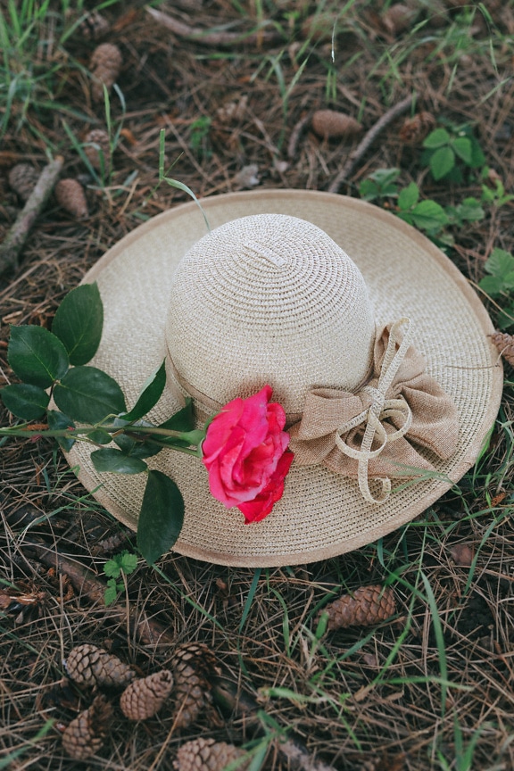 Handmade straw hat on ground with a pink rose on it
