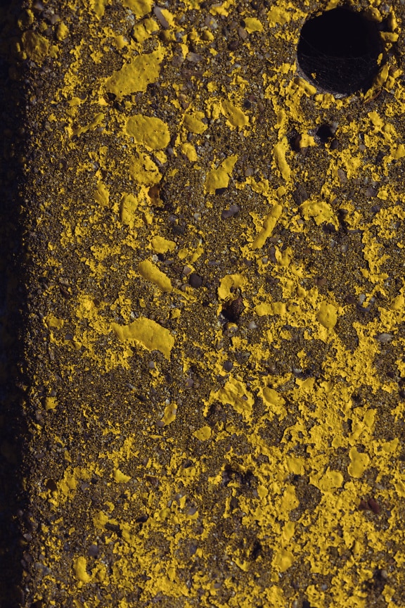 Peeling yellow paint on a rough concrete surface close-up