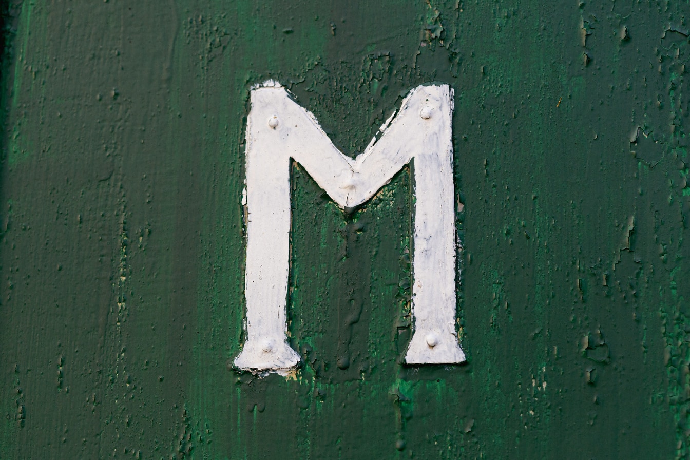 白色字母 (M) 在金属表面上，带有剥落的深绿色油漆